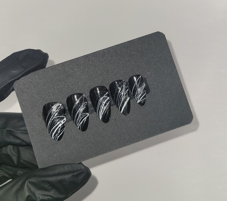 May include: Set of six black and white false nails with a white swirl design.