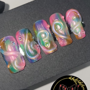 May include: Five iridescent pink, green, and gold swirl nail tips with a clear gel top coat. The tips are arranged in a row on a black surface.