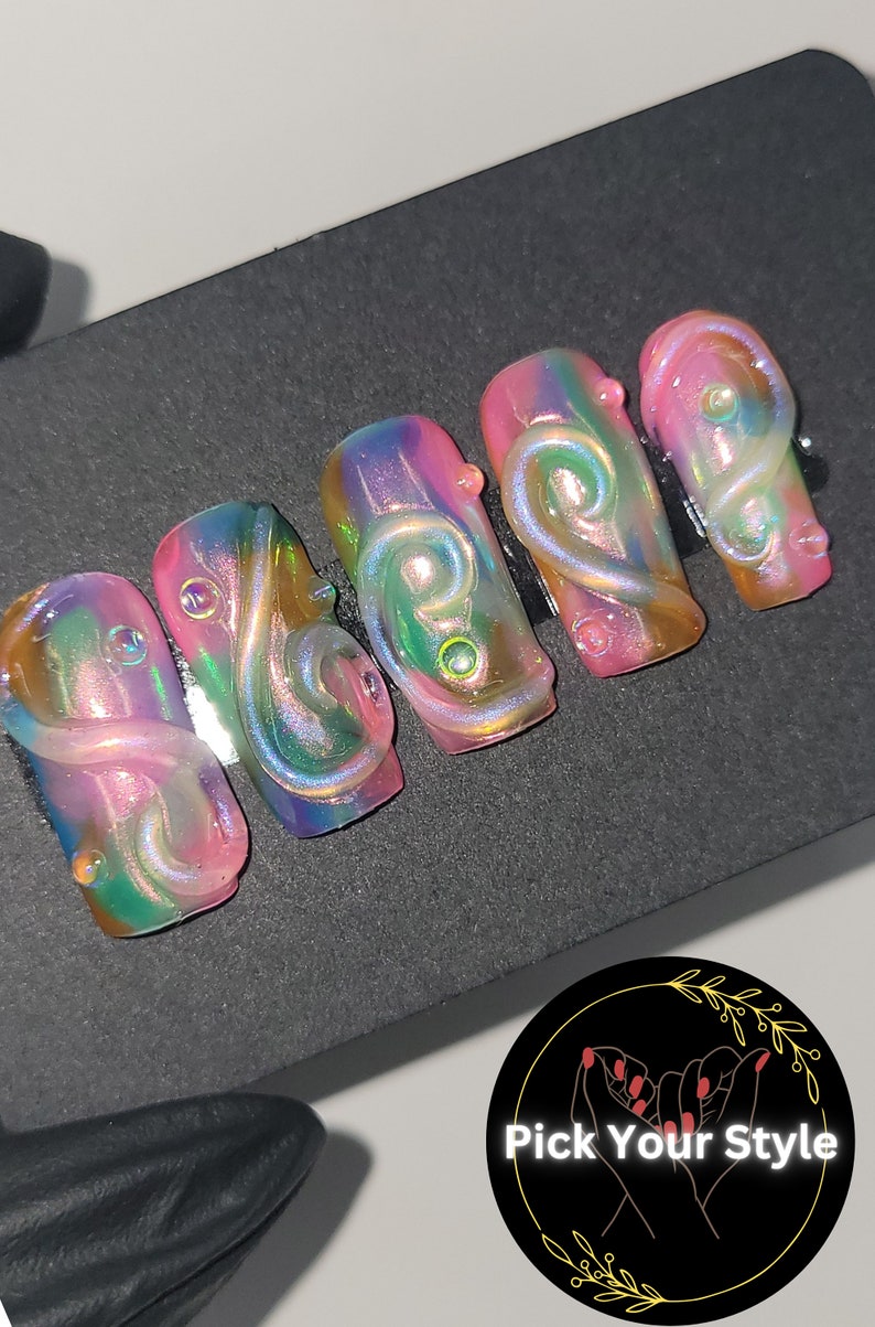 May include: Five iridescent pink, green, and gold swirl nail tips with a clear gel top coat. The tips are arranged in a row on a black surface.