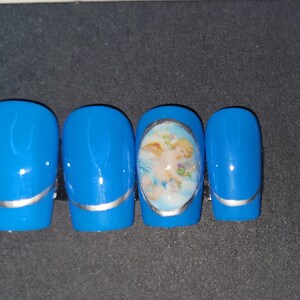 May include: Four blue press-on nails with a silver accent line. One nail features a round oval sticker with a cherub image.