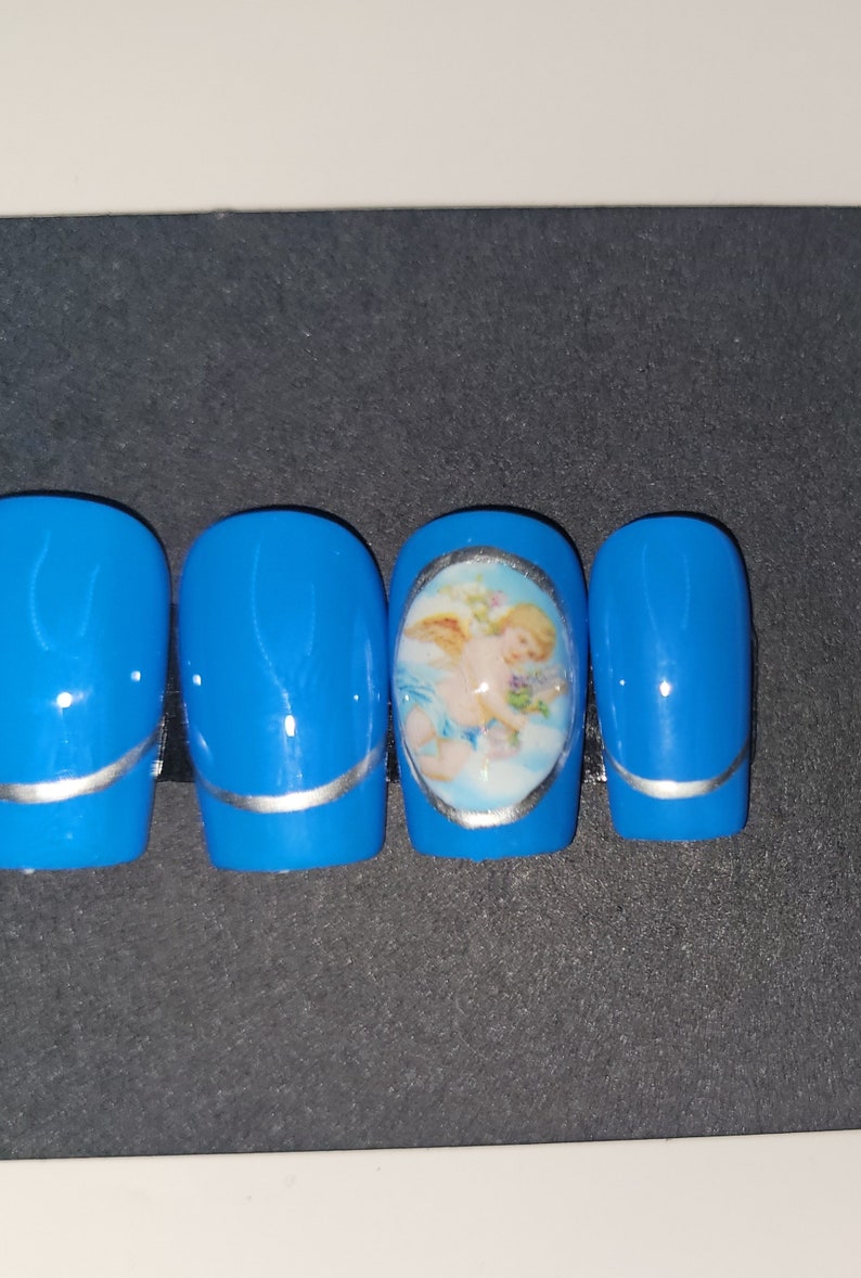 May include: Four blue press-on nails with a silver accent line. One nail features a round oval sticker with a cherub image.