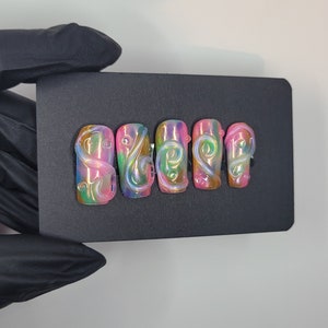 May include: Set of six false nails with a pink, green, and blue iridescent base and white swirl designs.