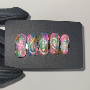 May include: Five iridescent pink and green press-on nails with a swirl design.