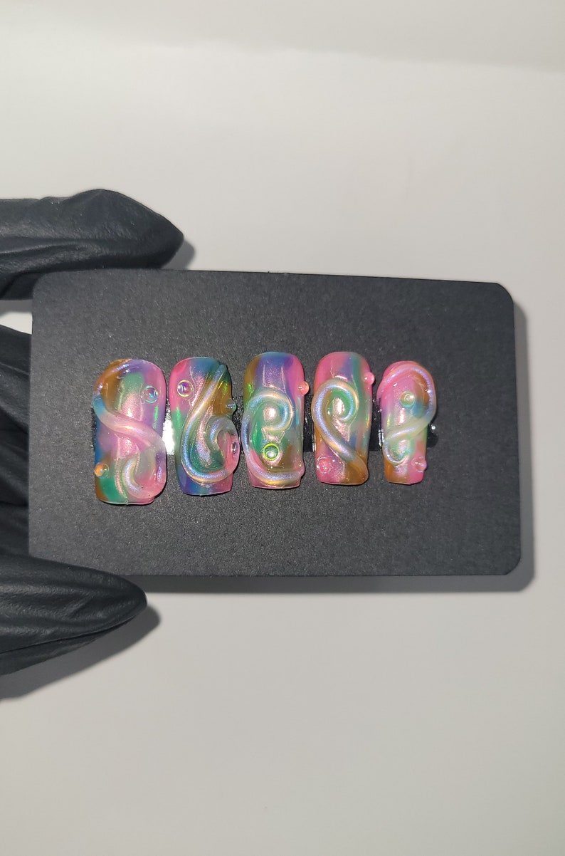 May include: Five iridescent pink and green press-on nails with a swirl design.