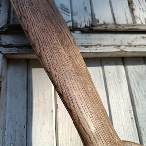 May include: A close-up of a wooden propeller with a dark brown stain. The propeller is made of wood with a grain pattern. The propeller is against a white wooden background.