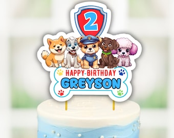 May include: Paw Patrol cake topper featuring the characters Chase, Marshall, Skye, Rocky, and Zuma. The topper includes a blue and white bone with the text "Happy Birthday Greyson" and a red shield with the number 2.