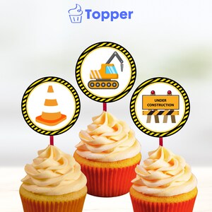 Op de afbeelding: Drie gele en oranje cupcakes met bouwthema toppers. De toppers zijn rond en bevatten een verkeerskegel, een bouwkraan en een bord met de tekst "In aanbouw".