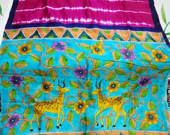 May include: A blue and pink silk saree with a hand-painted design of deer and flowers. The saree has a pink and white tie-dye pattern on the top half and a blue floral pattern on the bottom half. The saree is bordered with a green, orange, and blue geometric pattern. The saree is labeled "Rainbow Boutique".