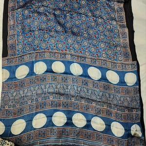 May include: A blue textile featuring a repeating pattern of circular floral motifs in the upper section. The lower section displays horizontal bands of intricate geometric and paisley designs interspersed with large, solid white circular shapes.