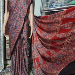 May include: A long, draped garment featuring a repeating geometric pattern in red, blue, and white. The fabric displays a dense grid of star-like motifs on the main body, transitioning to a large-scale leaf and circular pattern on the extended panel.