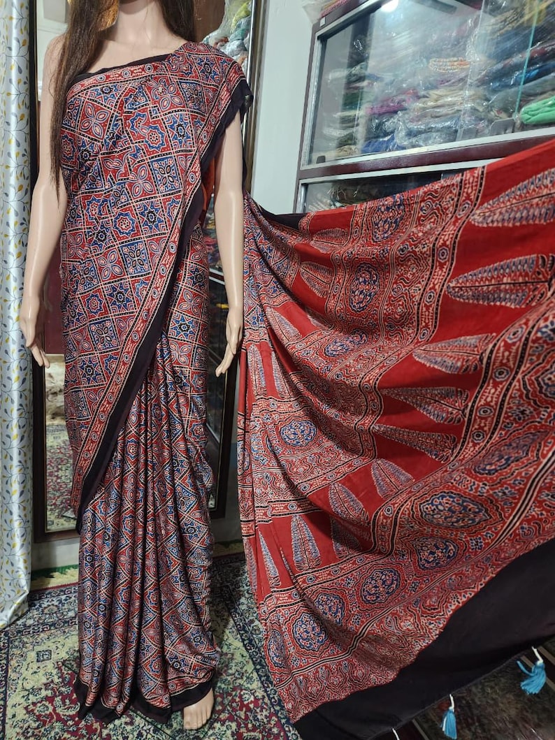 May include: A long, draped garment featuring a repeating geometric pattern in red, blue, and white. The fabric displays a dense grid of star-like motifs on the main body, transitioning to a large-scale leaf and circular pattern on the extended panel.