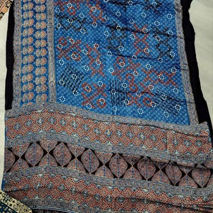 May include: A rectangular textile featuring a vibrant blue background with intricate white and rust-colored geometric patterns. The fabric displays a repeating motif of small stars, diamonds, and leaf-like shapes, finished with a wide decorative border.