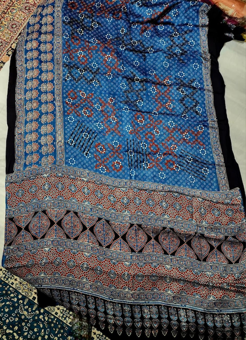 May include: A rectangular textile featuring a vibrant blue background with intricate white and rust-colored geometric patterns. The fabric displays a repeating motif of small stars, diamonds, and leaf-like shapes, finished with a wide decorative border.