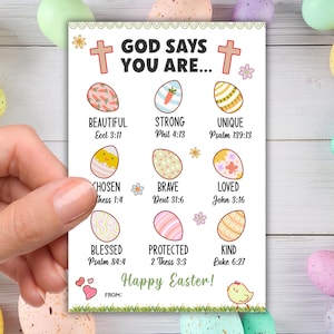 May include: A white card featuring the text "GOD SAYS YOU ARE..." and illustrations of decorated Easter eggs. The card also includes the words "Happy Easter!" and Bible verses. The card is held by a hand, with pastel Easter eggs in the background.