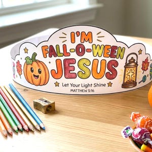 May include: A paper crown featuring the text I'M FALL-O-WEEN JESUS, Let Your Light Shine, and MATTHEW 5:16. The design includes a smiling orange pumpkin, a lantern, leaves, and candy illustrations. Colored pencils and a sharpener are nearby.
