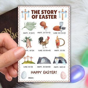 May include: A rectangular Easter-themed card with the text "THE STORY OF EASTER" and illustrations of religious symbols. The card includes the text "HAPPY EASTER!" and references to biblical verses. The card is held in a hand.