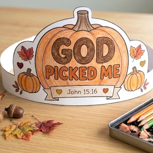 May include: A paper crown featuring a large central orange pumpkin illustration with the text GOD PICKED ME and John 15:16 printed on a banner. The design includes smaller pumpkins, autumn leaves, and hearts coloured in shades of orange and brown.