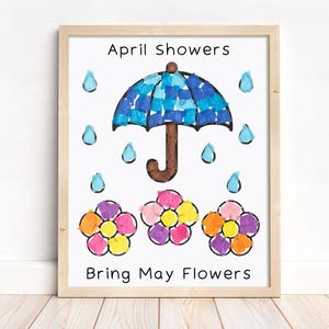 Puede incluir: Una impresi&oacute;n enmarcada con el texto "April Showers Bring May Flowers". La obra de arte presenta un paraguas azul, gotas de lluvia y flores coloridas. El marco es de madera clara.