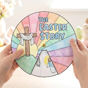 Peut inclure: Un artisanat coloré et circulaire de l'histoire de Pâques avec une croix en bois, un fond arc-en-ciel et le texte "The Easter Story". L'artisanat est tenu par des mains, avec un lapin et des œufs de Pâques en arrière-plan.