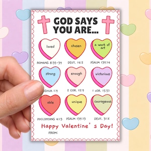 May include: A Valentine's Day card featuring the text "GOD SAYS YOU ARE..." and heart-shaped sweets with positive messages. The card, held by a hand, includes phrases such as "loved" and "chosen" and has a decorative border.