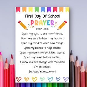 May include: A white card with the text "First Day Of School Prayer" and a prayer. The card has a colorful banner at the top and is decorated with pencils and hearts. The prayer is written in black text.