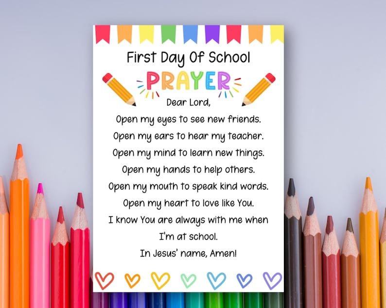 May include: A white card with the text "First Day Of School Prayer" and a prayer. The card has a colorful banner at the top and is decorated with pencils and hearts. The prayer is written in black text.