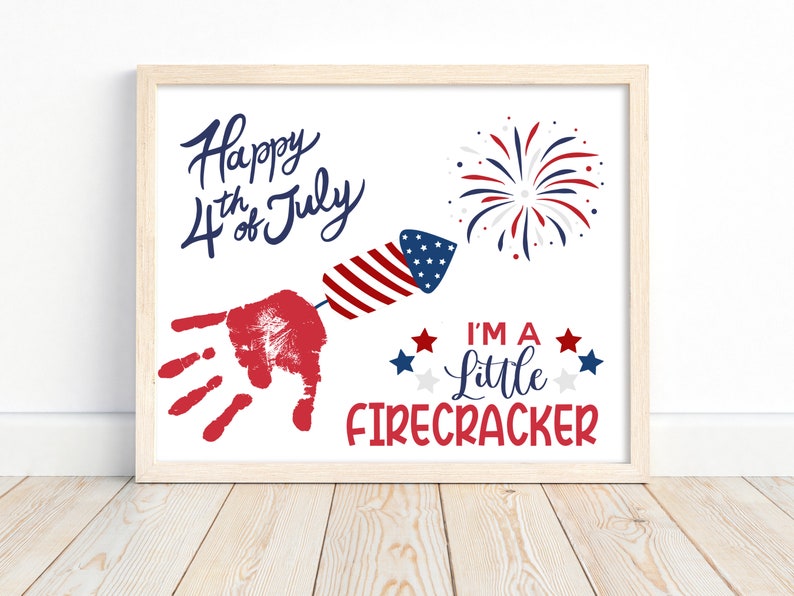 May include: A white framed print with the text "Happy 4th of July" and a red handprint with a red, white and blue firework rocket. The text "I'm a little firecracker" is below the handprint with red, white and blue stars.