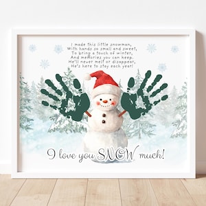 以下が含まれることがあります： 赤い帽子と手形のアームを持つ雪だるまが描かれた額入りのプリント。テキストは「I love you SNOW much！」と雪だるまについての詩です。背景には雪に覆われた森の風景が描かれています。