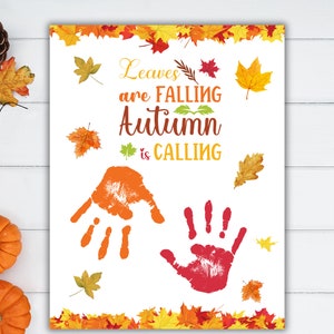 May include: A white printable sign with the text "Leaves are falling, Autumn is calling". The sign features two handprints, one orange and one red, surrounded by colorful fall leaves.