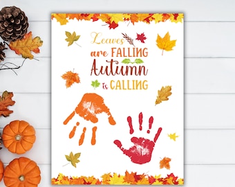 May include: A white printable sign with the text "Leaves are falling, Autumn is calling". The sign features two handprints, one orange and one red, surrounded by colorful fall leaves.