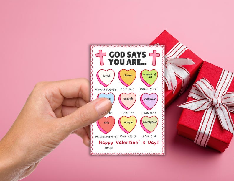 May include: A Valentine's Day card held by a hand, featuring a pink border and the text "GOD SAYS YOU ARE..." with various heart-shaped messages like "loved" and "unique." Two red gift boxes with white ribbons are in the background.