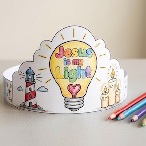 May include: A paper crown featuring a central yellow lightbulb illustration with the text "Jesus is my Light" and a pink heart. The crown includes drawings of a red and white lighthouse and three lit candles, accompanied by four colored pencils.