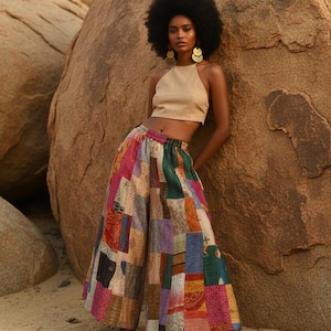 May include: A woman in a tan halter top and patchwork trousers. The wide-leg trousers are made of various colourful fabric patches. The woman is standing next to a large rock formation.