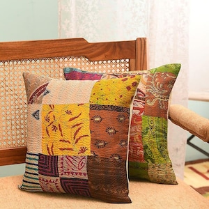 Könnte beinhalten: Zwei quadratische Kissen mit Patchwork-Designs. Die Kissen weisen eine Vielzahl von Farben auf, darunter Gelb, Braun, Grün und Lila. Die Kissen sind auf einem Holzstuhl mit gewebter Rückenlehne platziert.