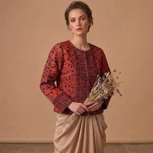 Könnte beinhalten: Eine langärmelige Jacke in leuchtendem Rot mit einem dichten schwarzen Blumen- und Paisle Blumen- und Paisleymuster. Das Kleidungsstück hat eine strukturierte Passform mit einer geraden Vorderöffnung und einem Band aus schwarzer Paisley-Stickerei.