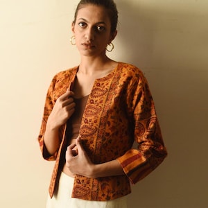 May include: An open-front, orange paisley jacket with three-quarter sleeves. The jacket features a detailed floral and paisley pattern in shades of orange, red, and brown. The sleeves have a striped design at the cuffs.