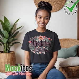 May include: A dark gray t-shirt with the text "Mockitos Mockups" surrounded by a floral design with pink and red accents. The model is wearing blue jeans and sitting in a wicker chair.