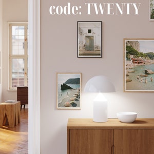May include: A white lamp with a mushroom-shaped shade sits on a wooden cabinet with three framed photos of beach scenes. The text "20% off when you buy 3+ prints with code: TWENTY" is displayed above the cabinet.