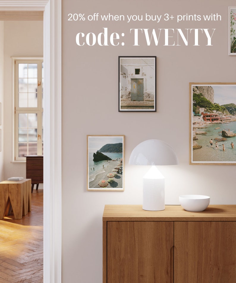 May include: A white lamp with a mushroom-shaped shade sits on a wooden cabinet with three framed photos of beach scenes. The text "20% off when you buy 3+ prints with code: TWENTY" is displayed above the cabinet.