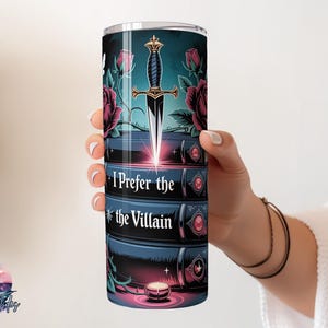 May include: A stainless steel tumbler featuring a design with a dagger, roses, and the text "I Prefer the Villain." The design is set against a dark teal background with a candle at the bottom. The tumbler is held by a person.