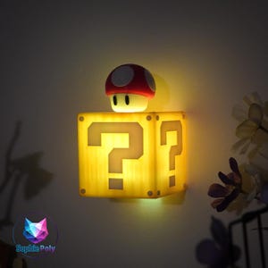 May include: A yellow, illuminated question mark block night light with a red and white mushroom on top. The night light is a cube shape with two question marks visible. The mushroom has a white base and red cap with white spots.