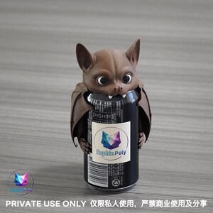 May include: A brown bat-shaped beverage can cooler featuring large eyes, pointed ears, and two small white fangs. The bat figure wraps around a black soda can with a white label displaying the text Sophie Poly and a geometric fox logo.