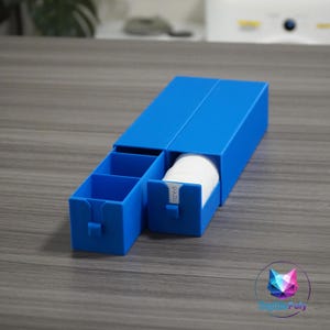 Puede incluir: Un organizador de almacenamiento de plástico azul brillante con dos cajones deslizantes. Un cajón está vacío con dos compartimentos internos, mientras que el otro está parcialmente abierto, revelando una pila de discos blancos con el texto PADS.