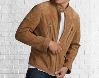 May include: A tan suede jacket with a stand-up collar and multiple zippered pockets. The jacket has a quilted shoulder detail and a front zipper closure. The person is wearing a white t-shirt underneath and blue jeans.
