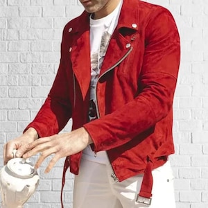 May include: A red suede jacket with a diagonal zipper and a belt detail. The jacket is paired with a white t-shirt and white pants. The background is a white brick wall.