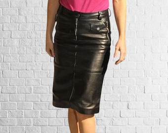 May include: A black leather pencil skirt with a front zip. The skirt has a fitted shape and falls to the knees. The skirt features a small pocket on the right side.