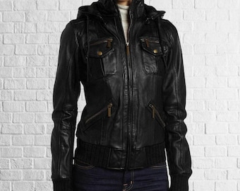 May include: A black leather jacket with a hood, multiple pockets, and a zipper closure. The jacket has a ribbed knit hem and cuffs. The jacket is worn over a gray turtleneck and blue jeans.