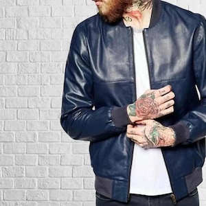 May include: A navy blue leather bomber jacket with a zip-up front and ribbed cuffs and hem. The jacket has a classic design and a sleek, modern look. The jacket is a versatile piece of outerwear.