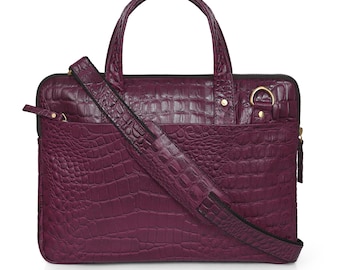 May include: A deep purple, textured leather laptop bag with a top handle and a detachable shoulder strap. The bag features a front pocket, a zipper closure, and gold-colored hardware. The bag has a crocodile skin pattern.