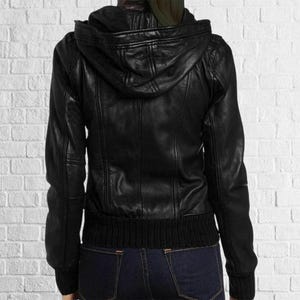 Puede incluir: Chaqueta de cuero negra con capucha, pu&ntilde;os y dobladillo acanalados. La chaqueta tiene cierre de cremallera y un dise&ntilde;o cl&aacute;sico. La chaqueta se muestra desde atr&aacute;s.